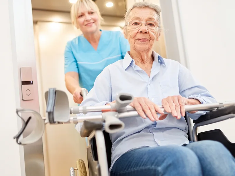 Caregiver assisting a stroke recovery patient who uses a wheelchair and forearm crutches