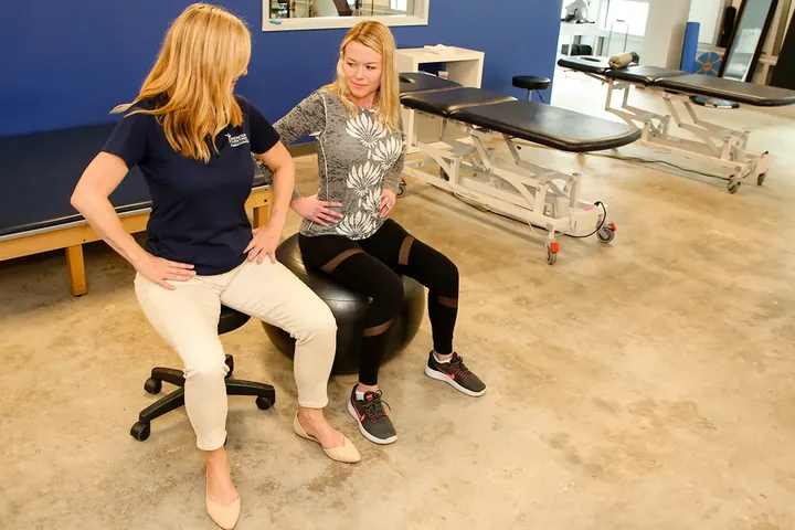 Therapist coaching a patient through a seated exercise on a stability ball